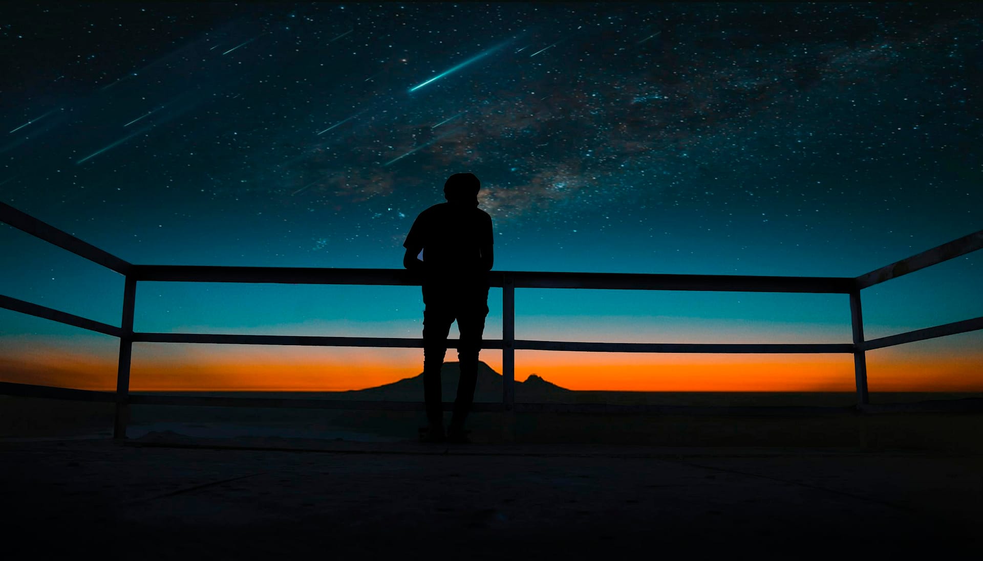 A silhouette of a person observing a vibrant night sky with stars and meteors.
